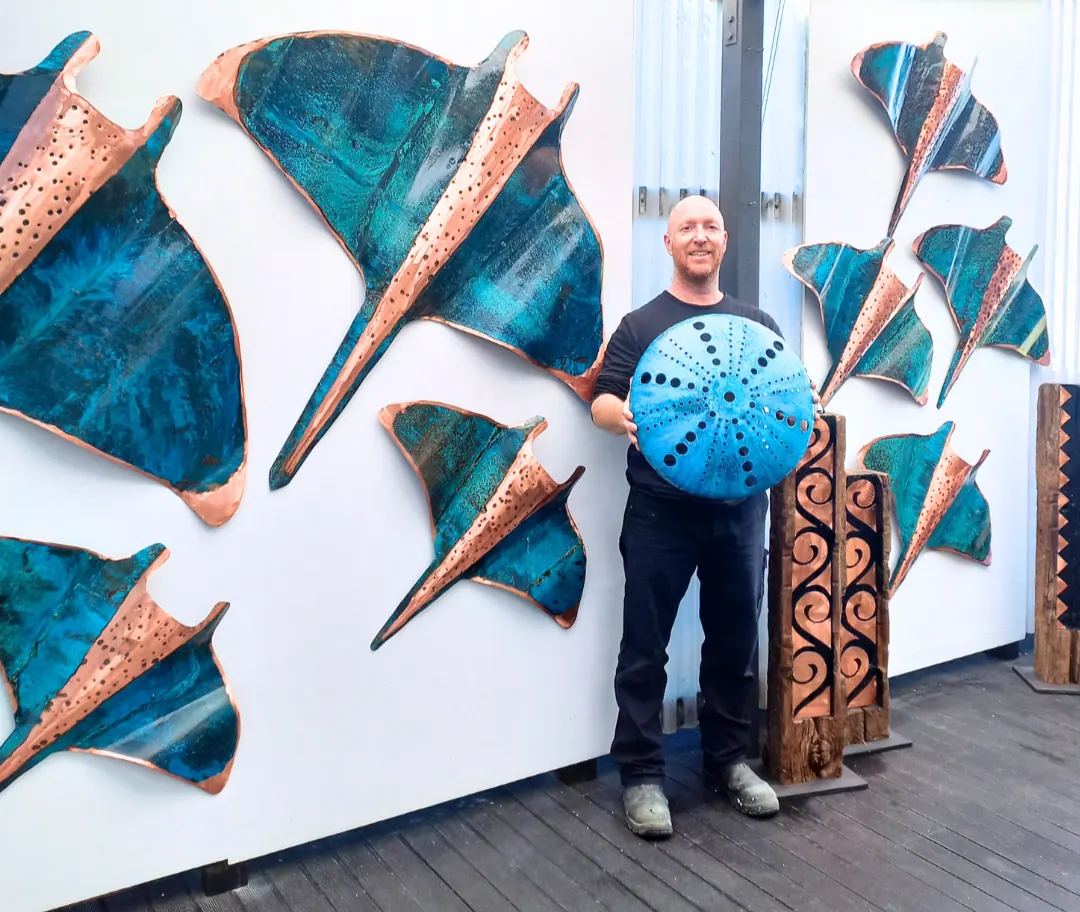 Isaac Weston beside a wall of copper manta rays and kina at an exhibition